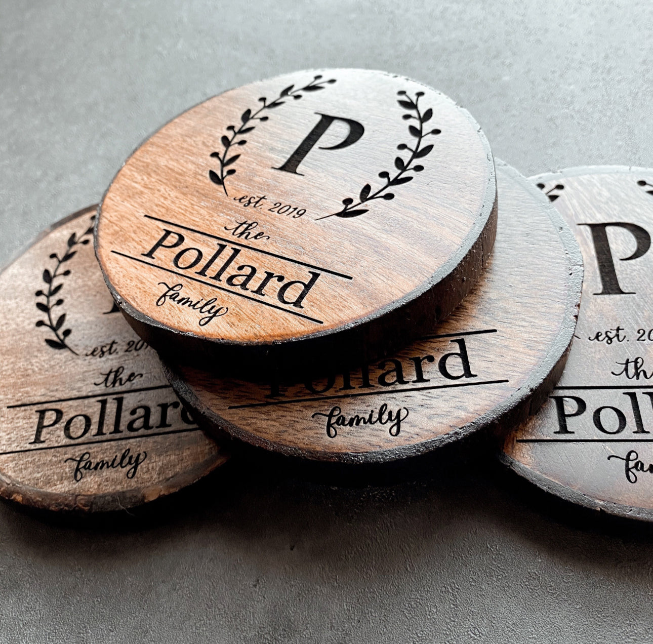Close-up of wreath monogram engraving with initial and family name on rustic wood slice coaster.