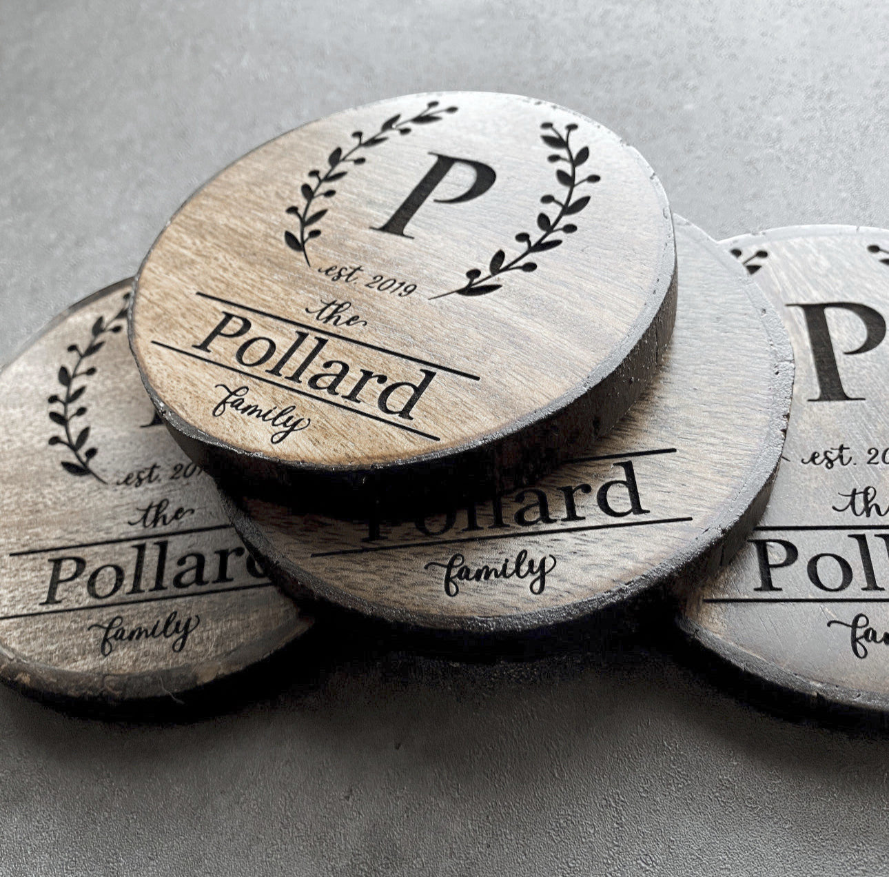 Close-up of wreath monogram engraving with initial and family name on rustic wood slice coaster.
