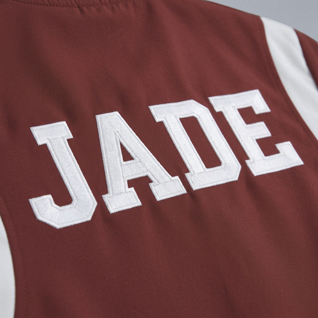 Rejecting Retail Studio personalized women's red varsity bomber jacket with white embroidered name "JADE" and white sleeve accents.
