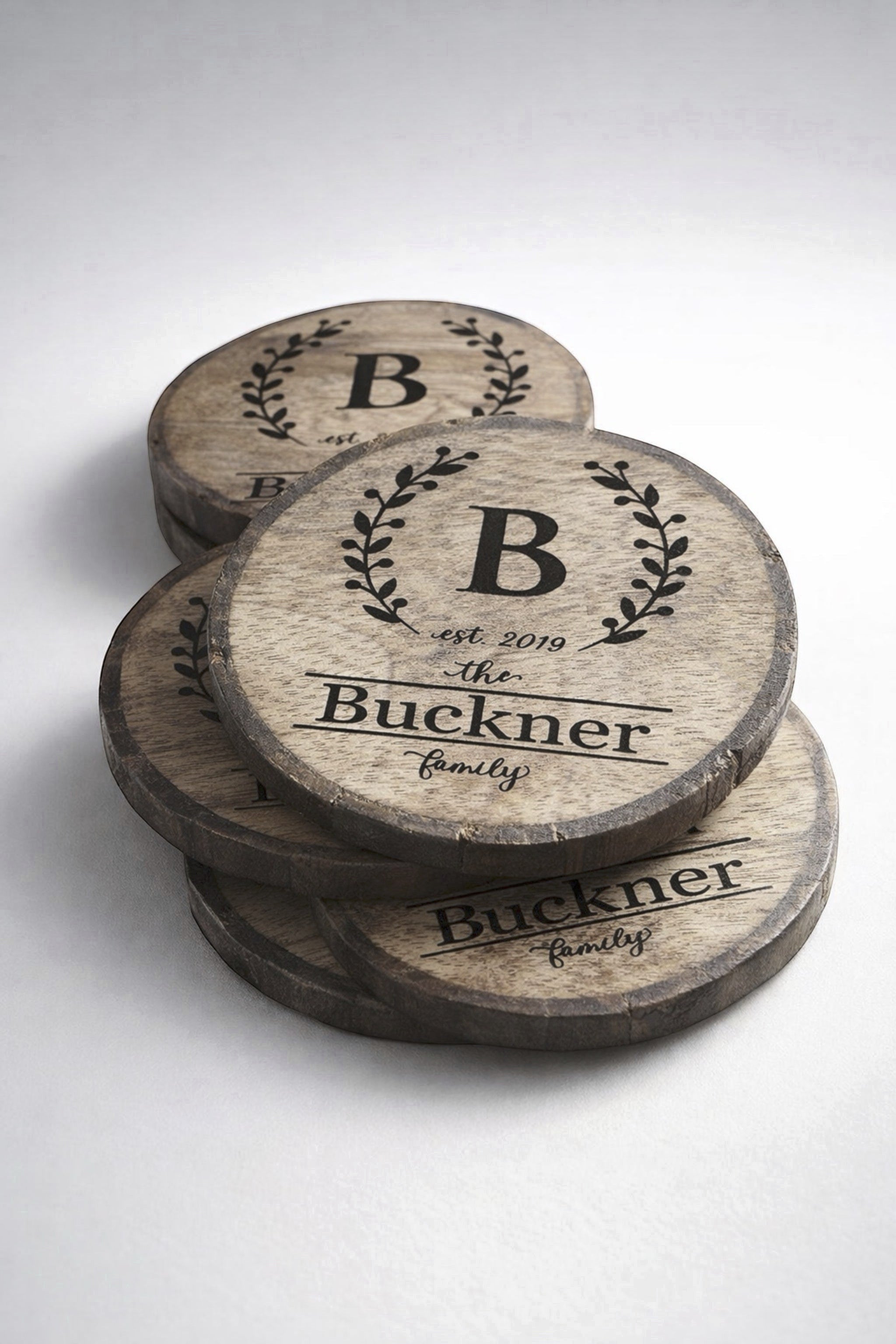 Close-up of wreath monogram engraving with initial and family name on rustic wood slice coaster.