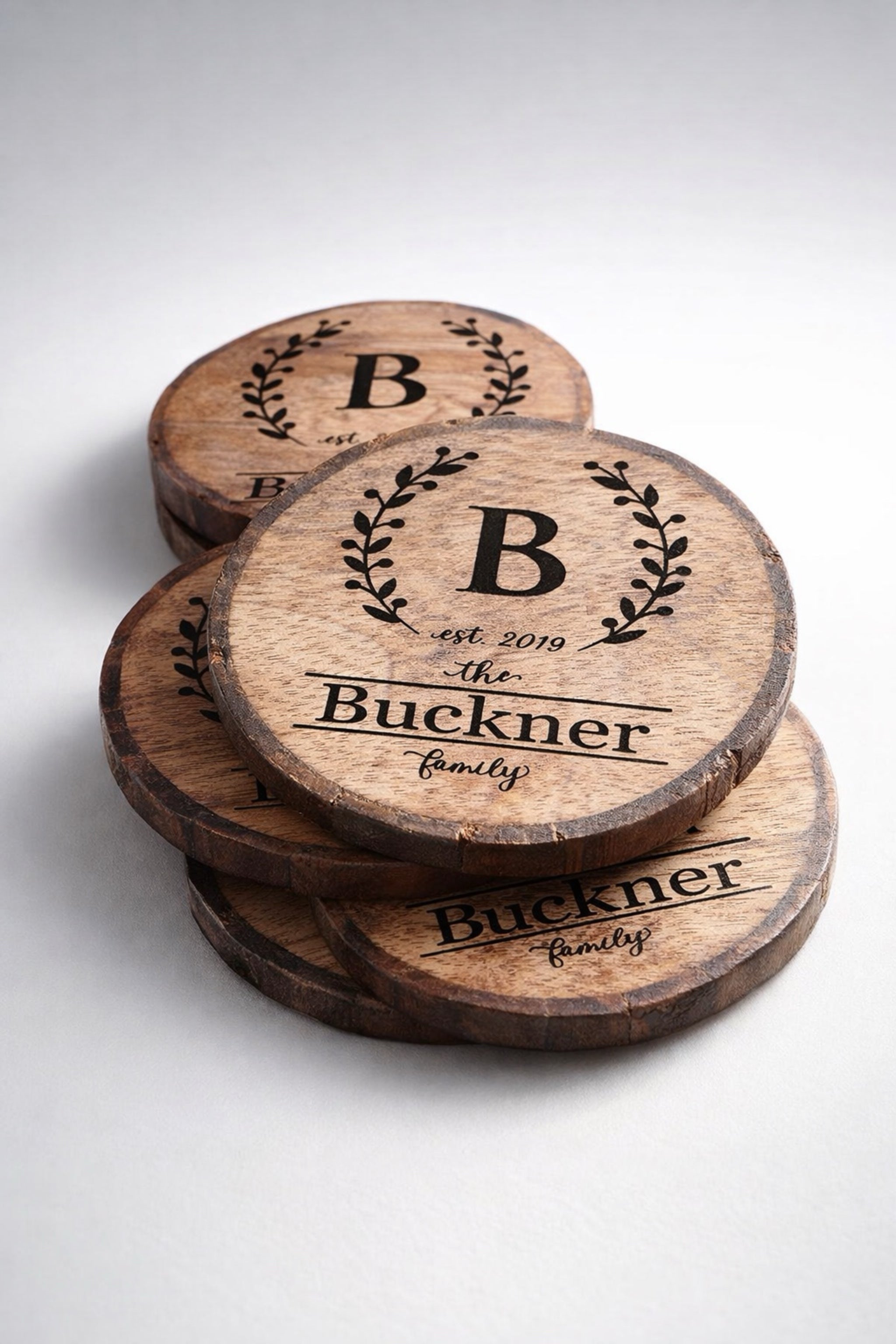Close-up of wreath monogram engraving with initial and family name on rustic wood slice coaster.