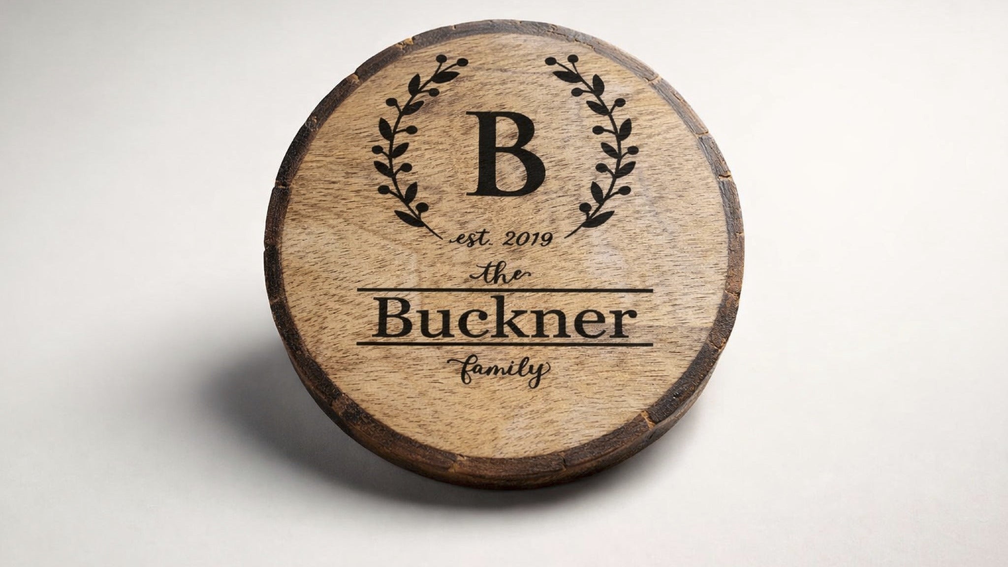 Personalized engraved wood coaster with wreath monogram and family name on natural wood slice.