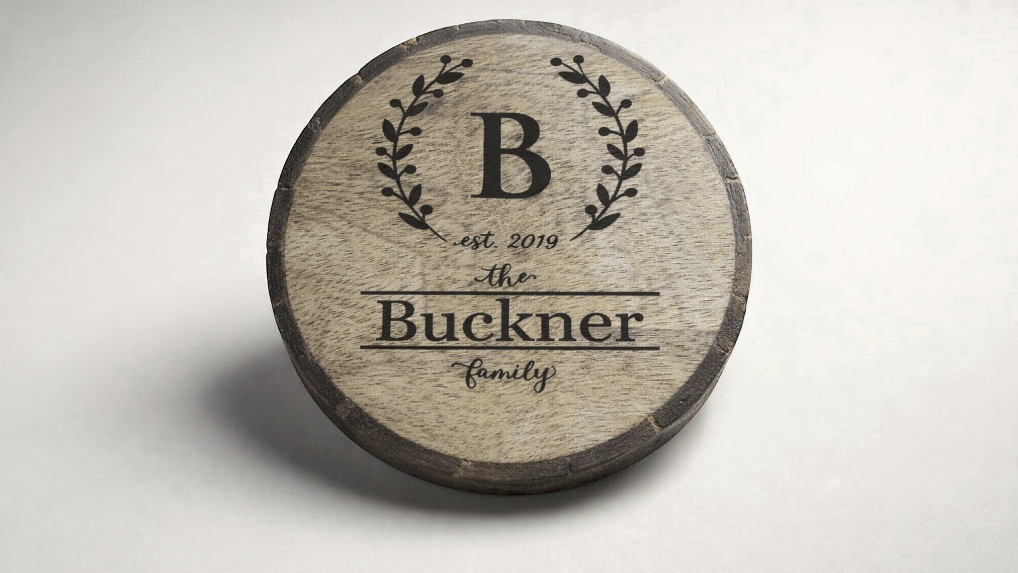Personalized engraved wood coaster with wreath monogram and family name on natural wood slice.