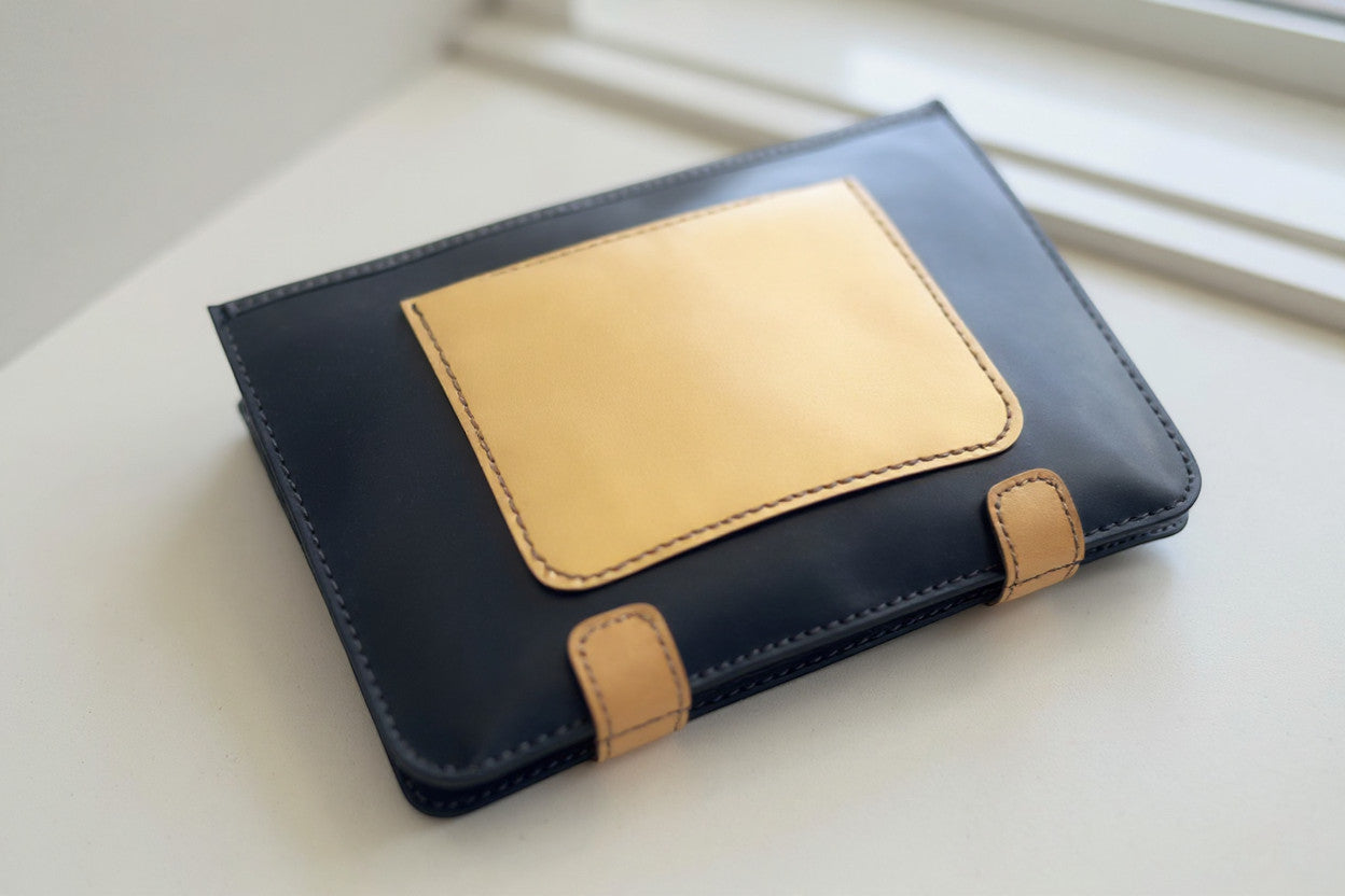 Rejecting Retail Studio black leather portfolio bag with tan leather accent pocket and hand-stitched details.