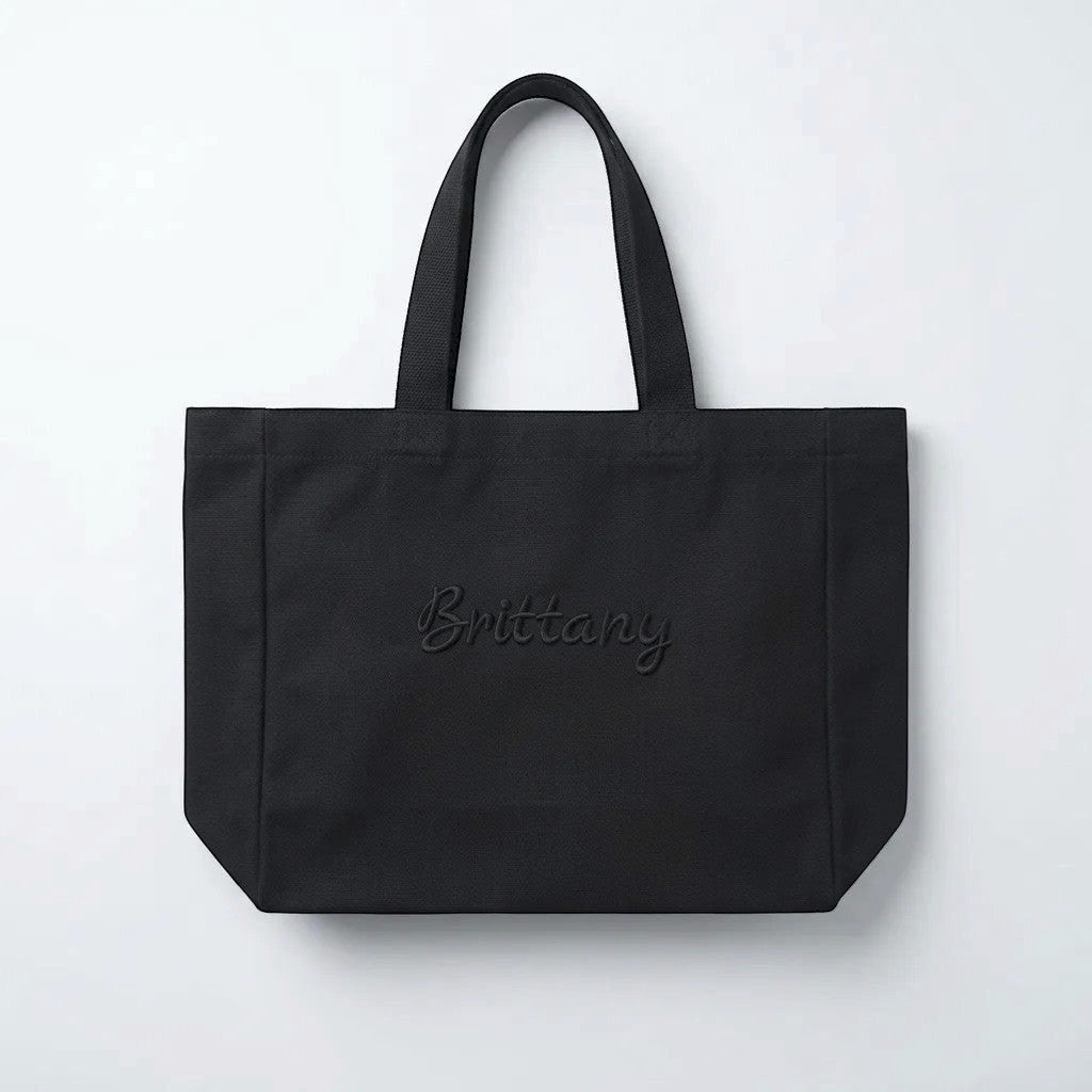 Rejecting Retail Studio black canvas tote bag with 3D puff embroidered custom name in script font.