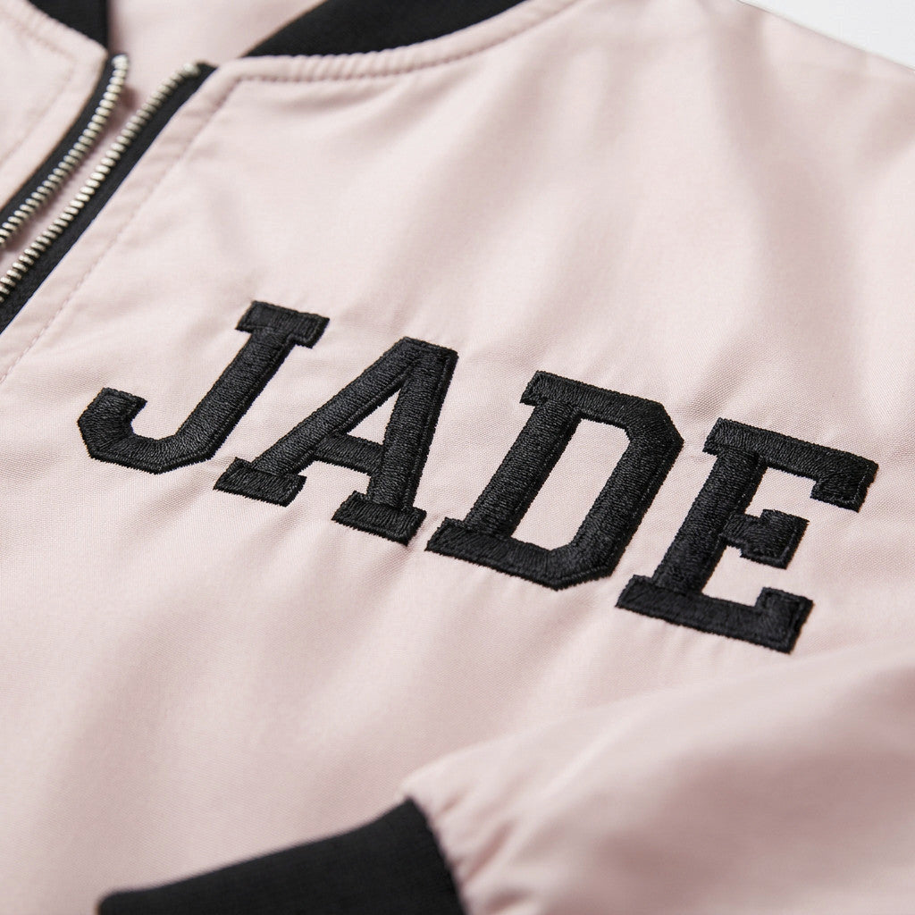 Rejecting Retail Studio pink satin zip-up varsity bomber jacket with custom black embroidered "JADE" lettering.